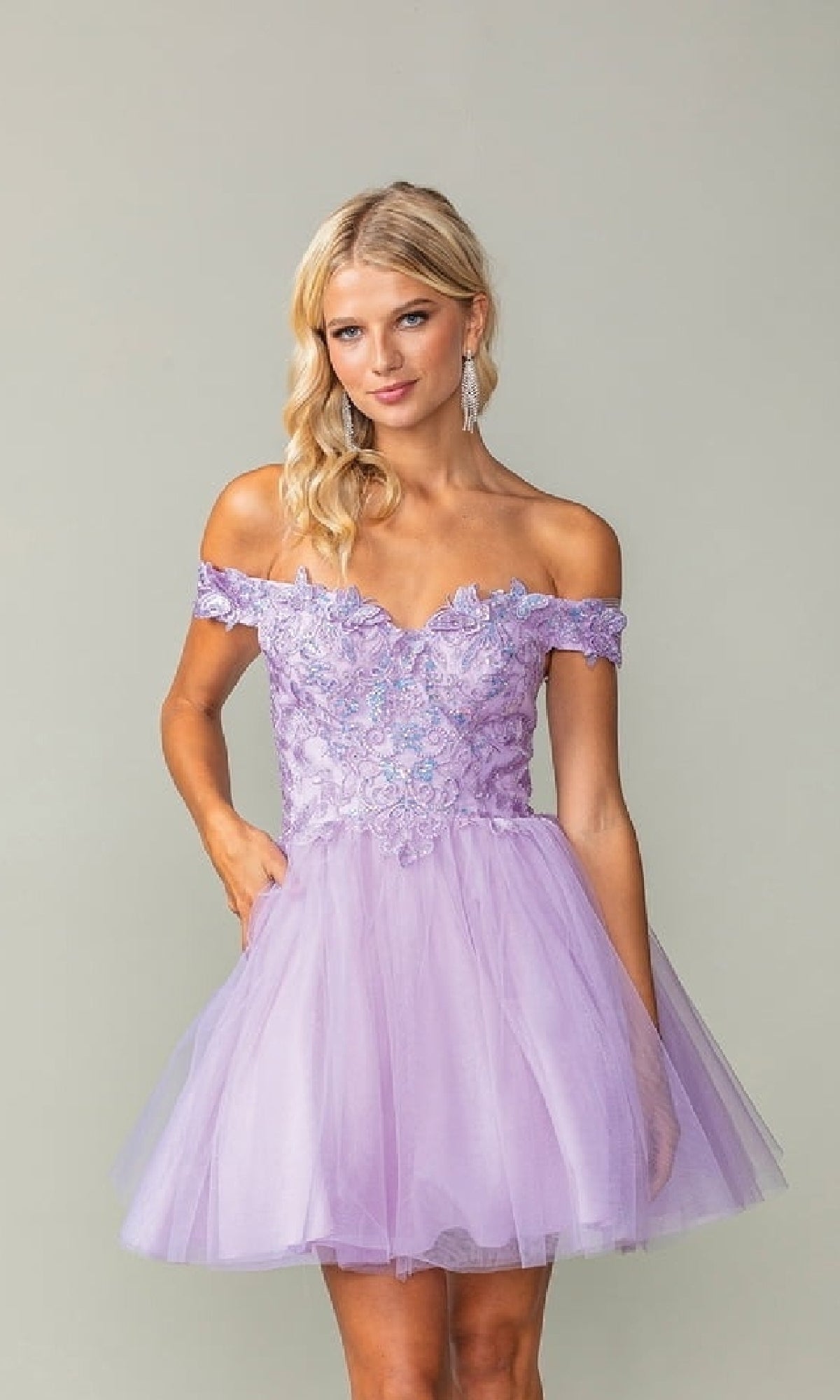 Woman wearing a short lilac purple off-shoulder dress with lace details on a plain background